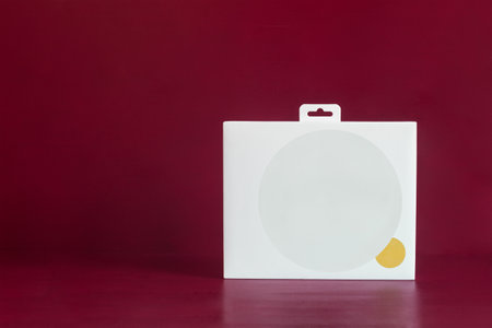 A white cardboard box with a large blank gray circle and a small gold one on a colorful red studio background and copy space. Storage, delivery, and shipping concept.の写真素材