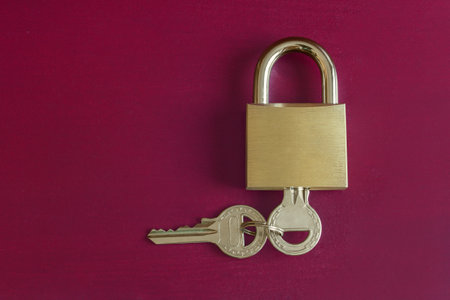 A gold padlock with a key inside and another key attached to it on a colorful studio background with copy space. Security and trust concept.の写真素材