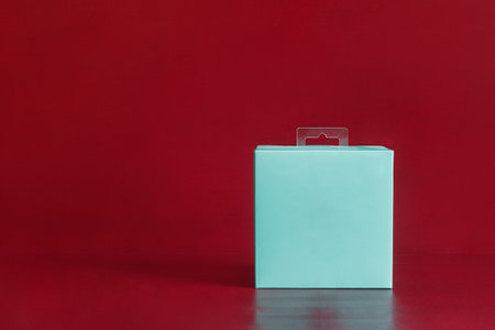 A blank blue square cardboard package box on a colorful red studio background with copy space. Gift, delivery, and shipping concept.の写真素材