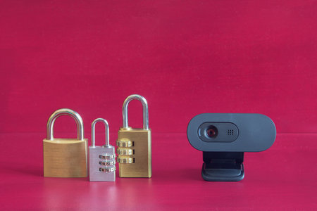 A webcam on its stand and three different locked padlocks on a colorful red studio background....