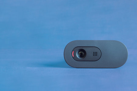 A webcam with the red light on ready to record on a colorful blue studio background with copy space. Security, technology, and entertainment.の写真素材