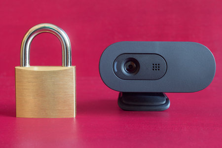 Close-up of a wireless webcam next to a closed old-fashioned gold padlock on a colorful red...