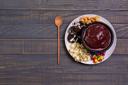 AÃ§ai Bowl with cookies, chocolate slices, nuts and coated chocolate on a woonden black background with copy spaceの写真素材