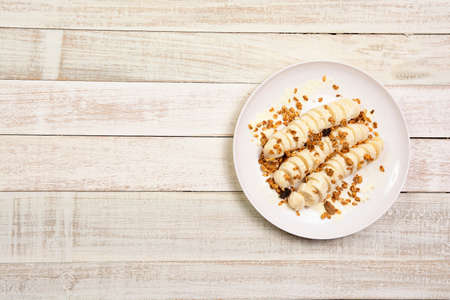 Banana slices with Granola in plate over white wood background with copy space. Healthy natural...