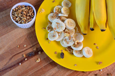 Slice Banana with Granola, Cereal on a yellow plate on a rustic wooden background with copy space,...