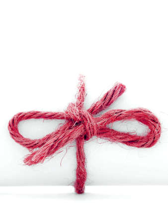 Handmade red cord knot tied on white message tube, isolated