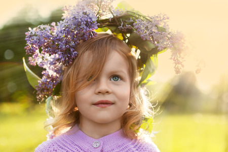 Little summer girl in lilac flowers garland in warm sunset sun rays on the meadowの写真素材