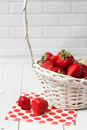 Ripe strawberry in the white basket with red polka-dot napkin on the light grey brick and wooden backgroundの写真素材