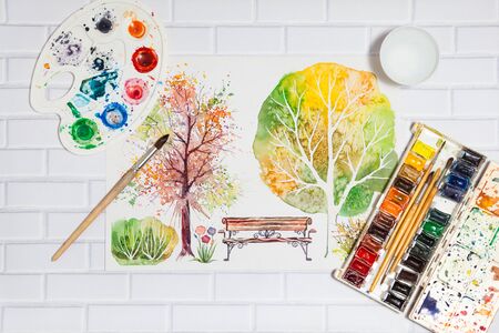 Hand Drawn Bright Sketch with autumn trees, bench, bush and lying flat paints, paintbrushes and palette on the white brick background - concept of human creativity, top viewの写真素材
