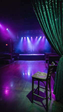 Empty stage with stool and mic under purple and blue lights. A moody venue setup for solo performance, ideal for stand-up, spoken word, or live acoustic show in evening setting.の素材