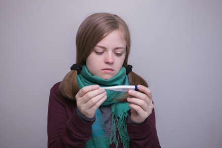 Young caucasian woman is sick and keeps a thermometer in her hands