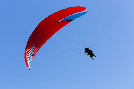 A silhouette of a paraglider with red chute floating across the blue skyの写真素材