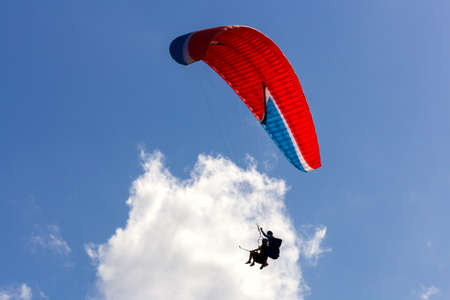 Tandem paragliders with red chute floating across white cloudの写真素材