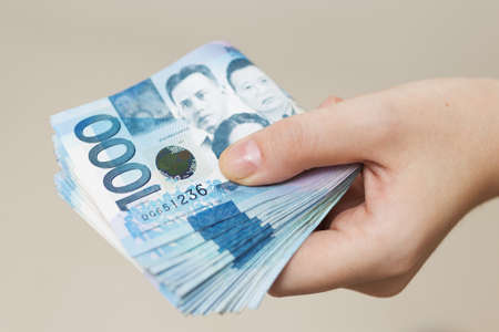 Hand holding folded bundle of blue money in cash of one thousand Philippines peso. Giving bribe, paying bills or getting salary. Payment day!の写真素材