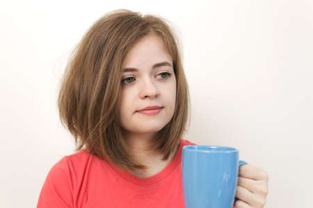 Portrait of young caucasian woman girl, yawning, tired or sleepy with bushy disheveled hair holding a mug of coffeeの写真素材