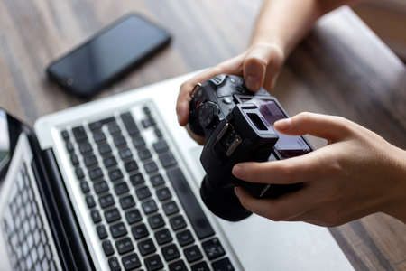 Photographer or stock photography concept, digital black camera in hands near laptop close upの写真素材