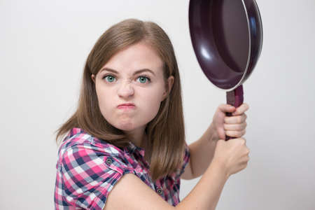 Young caucasian girl woman threaten to hit with frying pan. Angry, defensive or aggressive