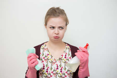 Unhappy sad young caucasian girl woman with rubber gloves, sponge and sprayer, cleaning the houseの写真素材