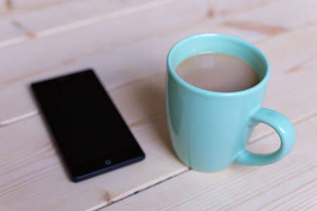Cup with coffee tea and phone on wooden surface, close up. Good morning!