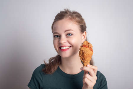 Smiling young Caucasian woman girl holding eating fried chicken  drumstickの写真素材
