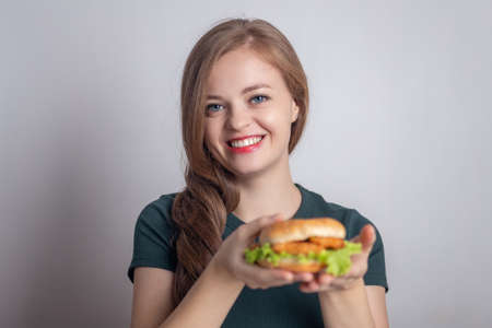 Smiling young Caucasian woman girl holding eating chicken burgerの写真素材