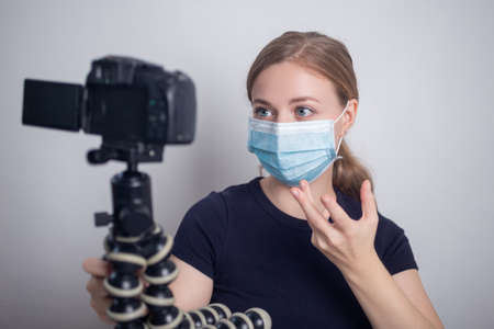 Young caucasian girl woman wearing mask, making a video blog (vlog) with camera at homeの写真素材