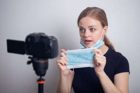 Young caucasian girl woman wearing mask, making a video blog (vlog) with camera at homeの写真素材