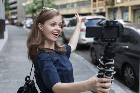 Smiling young caucasian girl woman making a video blog (vlog) with camera outside in the streetの写真素材