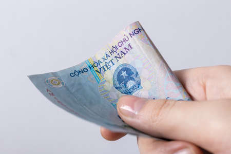 Hand holding cash banknote of  Vietnamese dong VND paying bills, payment procedure or bribe, salaryの写真素材