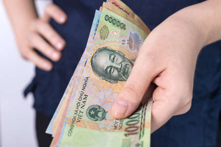 Hand holding cash banknote of  Vietnamese dong VND paying bills, payment procedure or bribe, salaryの写真素材