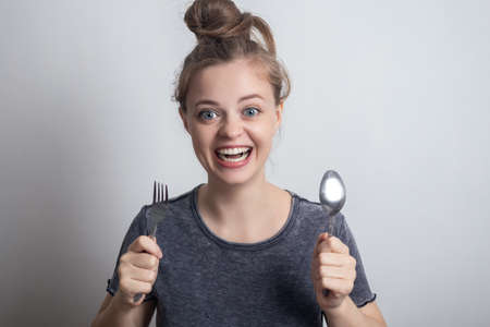 Young caucasian woman girl with spoon and fork in hands, looking excited and hungry. Funny face...