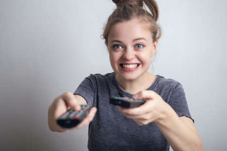 Smiling young caucasian woman holding two tv remote controls, enjoy watching movies. Funny excited faceの写真素材