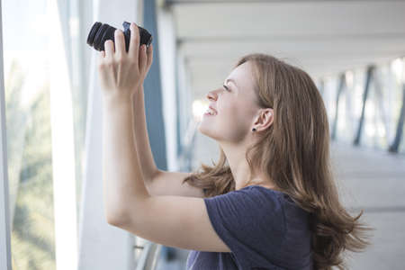 Young caucasian woman girl photographer holding a digital camera in hands, taking a photo or videoの写真素材