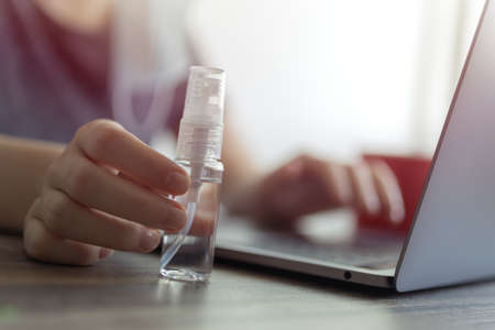 Close up of a hand with sanitizer alcohol bottle near laptop. Coronavirus covid-19 prevention at workplace or home during quarantineの写真素材