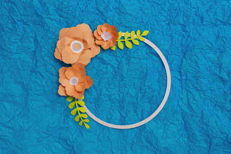 Round frame with orange color paper flowers on blue background. Flat lay, copy space, floral artの写真素材
