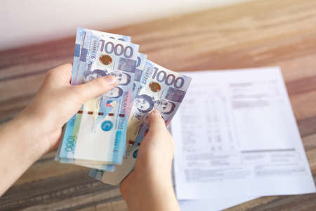 Hands holding cash banknote of one thousand Philippines peso paying bills, payment or salary.  White...