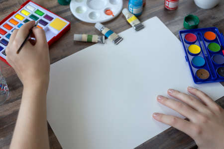 Close up of hands drawing painting with watercolor set on white paper with copy space. Art studio...
