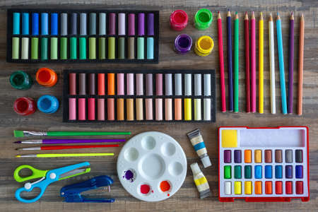 Colorful stationery flat lay: pastel crayons, colored pencils, watercolors on wooden background. Art workspace school concept. Top viewの写真素材
