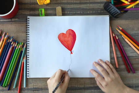 Flat lay of hands drawing a heart with colored pencils on white paper. Art studio workplace conceptの写真素材