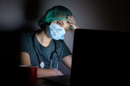 Caucasian woman doctor nurse in surgical mask looks tired, exhausted at night because of covid