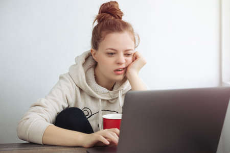 Young Caucasian woman looking bored in front of laptop at home. Work from home conceptの写真素材