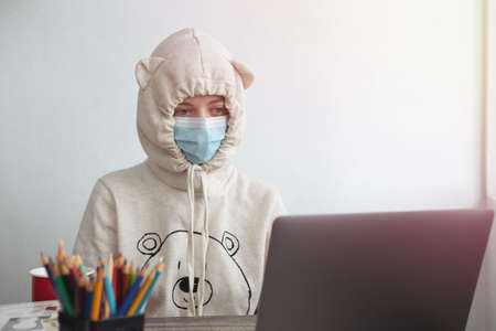 Young woman girl wearing mask and funny hoodie looking bored in front of laptop at home. Work from home during covid quarantine conceptの写真素材