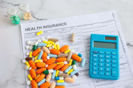Colorful medicine pills on insurance paper bill and blue calculator. Health care cost conceptの写真素材