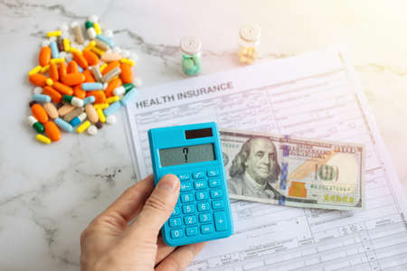 One hundred us dollar on insurance paper bill, calculator and medicine pills. Health care cost conceptの写真素材