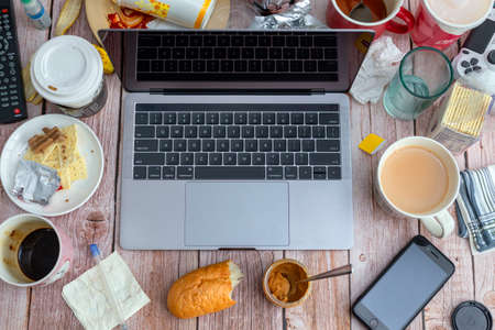 Working from home concept. View from above to workplace with a laptop stuffed with empty utensils, garbage and other things.のeditorial素材