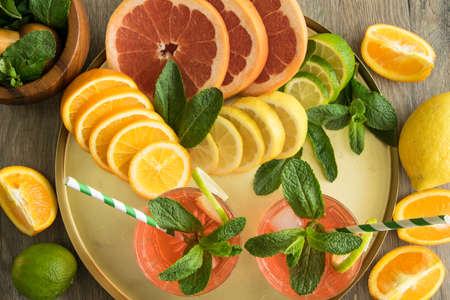 Top view of sliced juicy citrus fruits and two glasses of summer lemonade, cocktail with straw, ice...