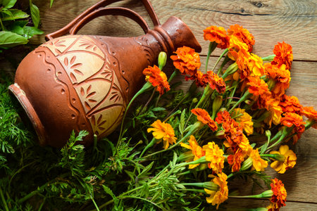 Top view colorful orange flowers, ornamental clay jar on wooden table indoors. Beautiful yellow bouquet of marigolds and erthenware jar. Traditional still life pattern. Background concept. Copy spaceの写真素材