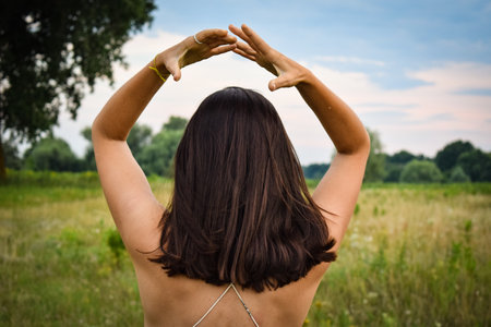 Rear view multiracial young woman stands at picturesque meadow, embracing romance of twilight. Scenic beauty of meadow complements enchanting atmosphere of dusk creating captivating and romantic sceneの写真素材