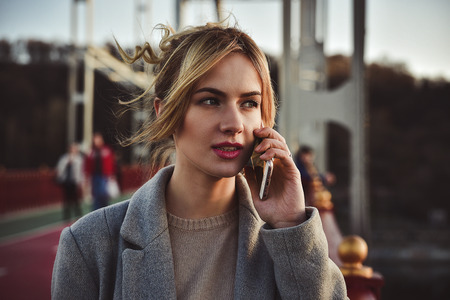 Cute smiling young woman talking on phone standing on the bride. Close up portrait