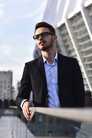 Modern businessman. Confident young man in full suit standing outdoors with cityscape in the backgroundの写真素材